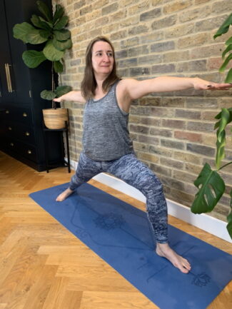 woman on blue yoga mat doing warrior 2 yoga pose